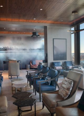 A modern lounge with plush seating, large windows offering a scenic view of the cityscape and water, and stylish decor within a cozy ambiance.