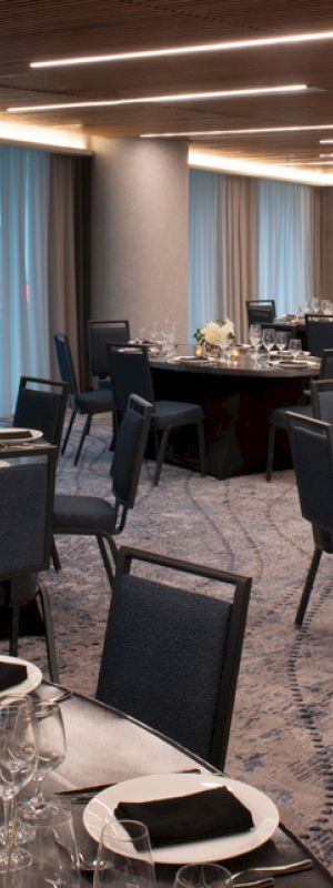The image shows an elegantly set banquet hall with round tables, chairs, plates, glasses, and floral centerpieces under soft lighting.