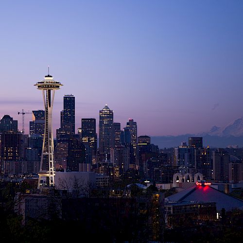 Seattle skyline at dusk with the Space Needle and Mount Rainier in the background under a clear purple sky.